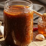 Hot Honey BBQ Sauce – The Best Sweet & Spicy Recipe (2025) 2 Thick homemade hot honey BBQ sauce in a jar with fresh garlic, chili peppers, and honey