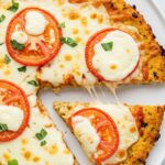 Chicken Crust Pizza : The Ultimate Low-Carb, High-Protein Delight 10 Thin chicken crust pizza topped with cheese and tomato slices, with one slice removed showing melted cheese.
